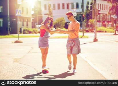 summer holidays, extreme sport and people concept - happy teenage couple riding short modern cruiser skateboard on city street. teenage couple riding skateboards on city street