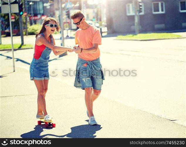 summer holidays, extreme sport and people concept - happy teenage couple riding short modern cruiser skateboard on city street. teenage couple riding skateboards on city street
