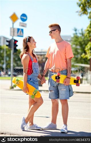 summer holidays, extreme sport and people concept - happy teenage couple with short modern cruiser skateboards talking on city street