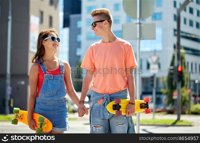 summer holidays, extreme sport and people concept - happy teenage couple with short modern cruiser skateboards on city street
