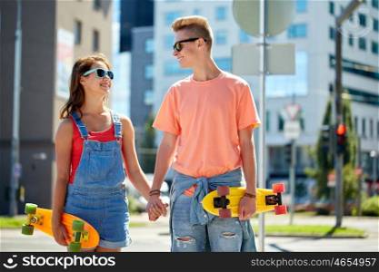 summer holidays, extreme sport and people concept - happy teenage couple with short modern cruiser skateboards on city street