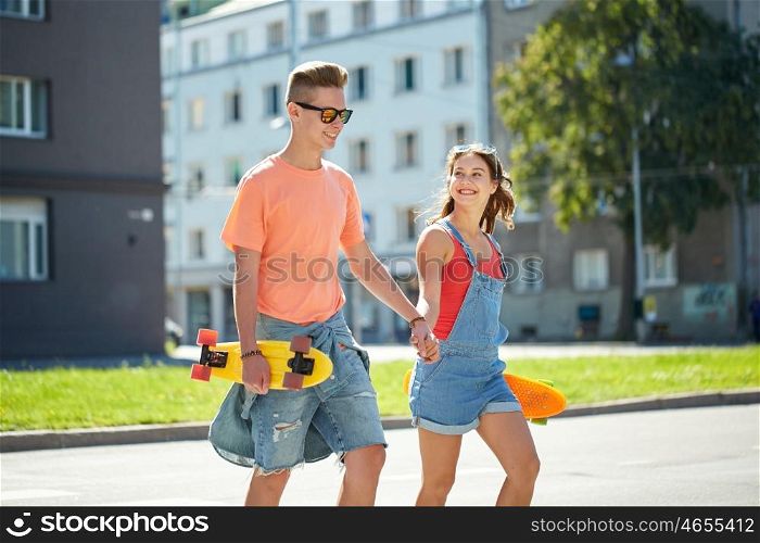 summer holidays, extreme sport and people concept - happy teenage couple with short modern cruiser skateboards crossing city crosswalk