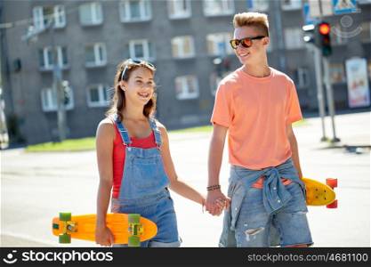 summer holidays, extreme sport and people concept - happy teenage couple with short modern cruiser skateboards walking along city street