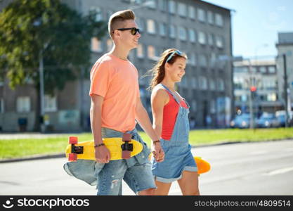 summer holidays, extreme sport and people concept - happy teenage couple with short modern cruiser skateboards walking along city street