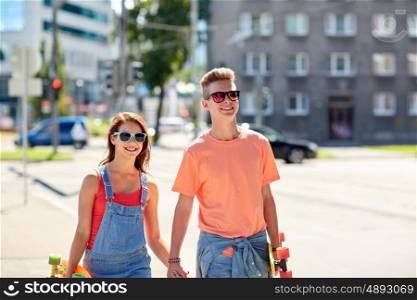 summer holidays, extreme sport and people concept - happy teenage couple with short modern cruiser skateboards walking along city street