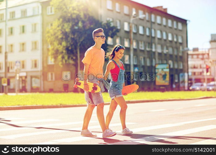 summer holidays, extreme sport and people concept - happy teenage couple with short modern cruiser skateboards crossing city crosswalk. teenage couple with skateboards on city street