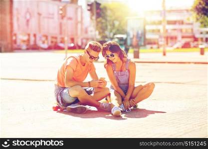 summer holidays, extreme sport and people concept - happy teenage couple with short modern cruiser skateboards on city street with smartphone. couple with skateboards and smartphone in city
