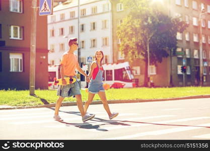 summer holidays, extreme sport and people concept - happy teenage couple with short modern cruiser skateboards crossing city crosswalk. teenage couple with skateboards on city street