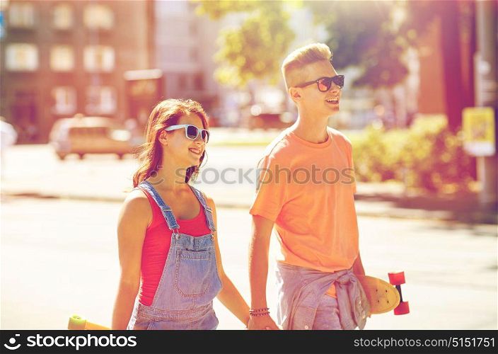 summer holidays, extreme sport and people concept - happy teenage couple with short modern cruiser skateboards walking along city street. teenage couple with skateboards on city street