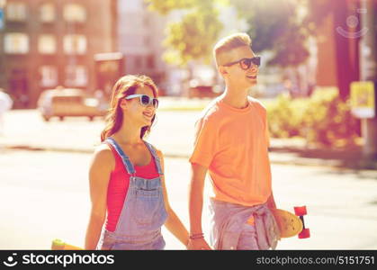 summer holidays, extreme sport and people concept - happy teenage couple with short modern cruiser skateboards walking along city street. teenage couple with skateboards on city street