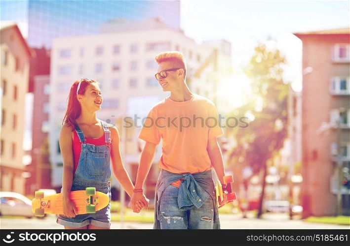 summer holidays, extreme sport and people concept - happy teenage couple with short modern cruiser skateboards on city street. teenage couple with skateboards on city street