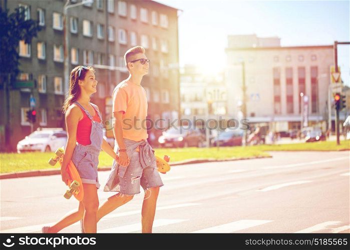 summer holidays, extreme sport and people concept - happy teenage couple with short modern cruiser skateboards crossing city crosswalk. teenage couple with skateboards on city street