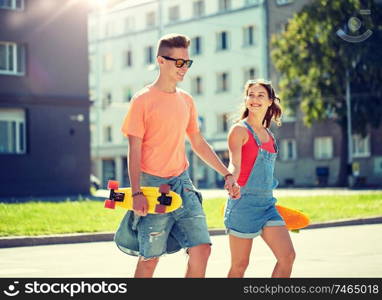 summer holidays, extreme sport and people concept - happy teenage couple with short modern cruiser skateboards crossing city crosswalk. teenage couple with skateboards on city street