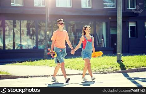 summer holidays, extreme sport and people concept - happy teenage couple with short modern cruiser skateboards crossing city crosswalk. teenage couple with skateboards on city street