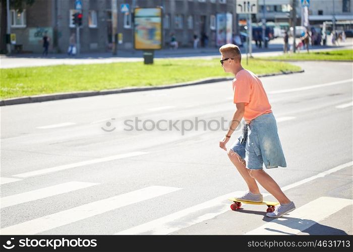 summer holidays, extreme sport and people concept - teenage boy riding short modern cruiser skateboard on crosswalk in city