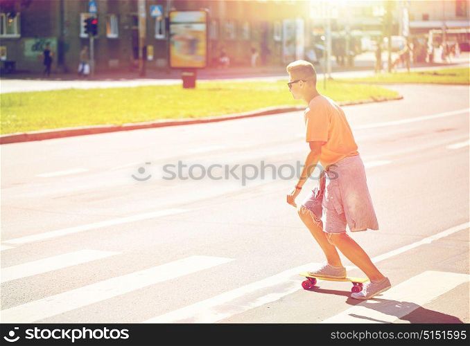 summer holidays, extreme sport and people concept - teenage boy riding short modern cruiser skateboard on crosswalk in city. teenage boy on skateboard crossing city crosswalk