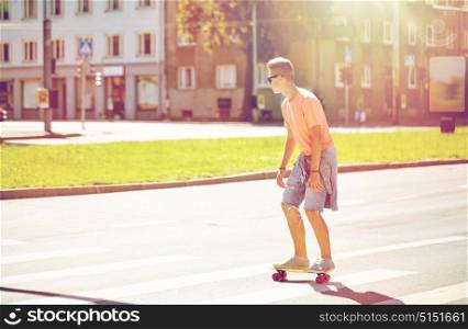 summer holidays, extreme sport and people concept - teenage boy riding short modern cruiser skateboard on crosswalk in city. teenage boy on skateboard crossing city crosswalk