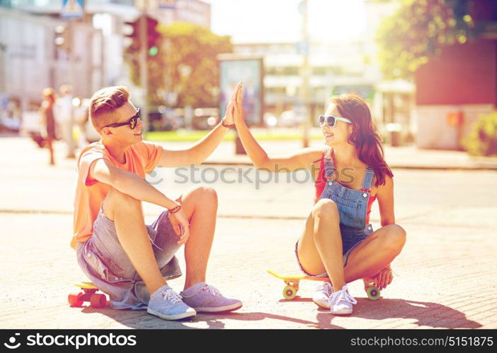 summer holidays, extreme sport, gesture and people concept - happy teenage couple with short modern cruiser skateboards on city street making high five. teenage couple with skateboards on city street