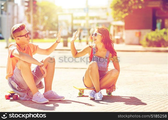 summer holidays, extreme sport, gesture and people concept - happy teenage couple with short modern cruiser skateboards on city street making high five. teenage couple with skateboards on city street