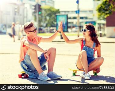 summer holidays, extreme sport, gesture and people concept - happy teenage couple with short modern cruiser skateboards on city street making high five. teenage couple with skateboards on city street
