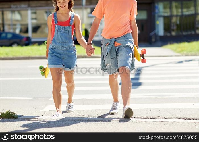 summer holidays, extreme sport, relations and people concept - happy teenage couple with short modern cruiser skateboards crossing city crosswalk
