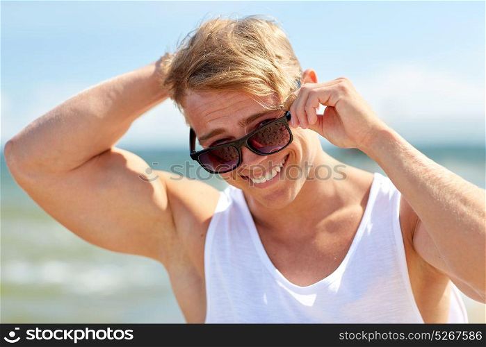 summer holidays, eyewear and people concept - happy smiling young man in sunglasses on beach. smiling young man in sunglasses on summer beach