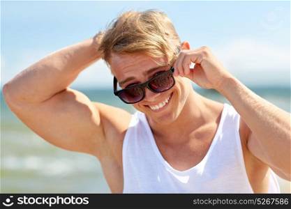 summer holidays, eyewear and people concept - happy smiling young man in sunglasses on beach. smiling young man in sunglasses on summer beach