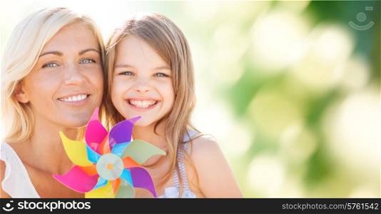 summer holidays, family, children and people concept - happy mother and girl with pinwheel toy over green background