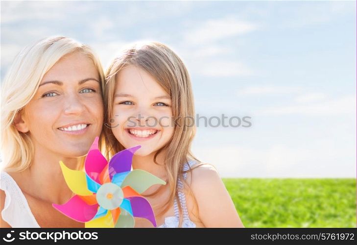 summer holidays, family, children and people concept - happy mother and girl with pinwheel toy over blue sky and grass background