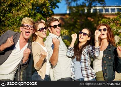 summer holidays, friendship, achievement and success concept - group of happy friends showing triumph gesture at campus or city park