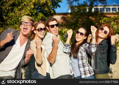 summer holidays, friendship, achievement and success concept - group of happy friends showing triumph gesture at campus or city park