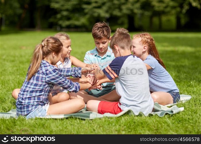 summer holidays, friendship, childhood, leisure and people concept - group of happy pre-teen kids putting hands together in park