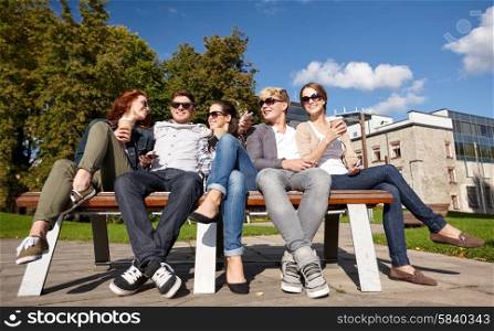 summer holidays, friendship, leisure and teenage concept - group of happy students or teenagers hanging out and drinking coffee at campus or park