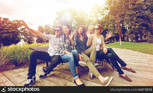 summer holidays, friendship, leisure and teenage concept - group of students or teenagers hanging out and waving hands at campus or park