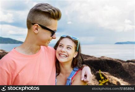 summer holidays, love and people concept - happy smiling teenage couple hugging and looking at each other over island and sea background. happy teenage couple hugging outdoors