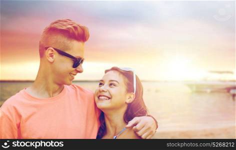 summer holidays, love and people concept - happy smiling teenage couple hugging over beach background. happy teenage couple hugging on summer beach