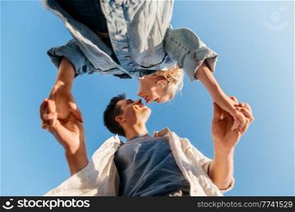 summer holidays, love and people concept - happy young couple holding hands under blue sky, from below. happy young couple holding hands under blue sky