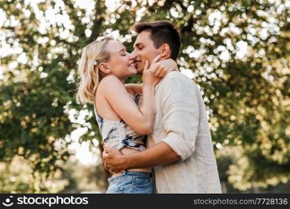 summer holidays, love and people concept - happy young couple kissing and hugging outdoors. happy young couple kissing and hugging outdoors
