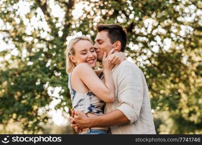summer holidays, love and people concept - happy young couple kissing and hugging outdoors. happy young couple kissing and hugging outdoors