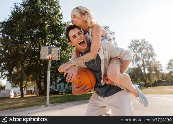 summer holidays, love and people concept - happy young couple with ball having fun on basketball playground. happy couple having fun on basketball playground