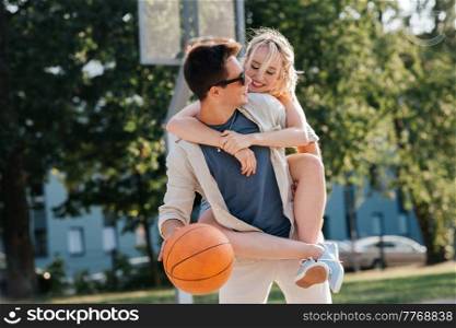 summer holidays, love and people concept - happy young couple with ball having fun on basketball playground. happy couple having fun on basketball playground