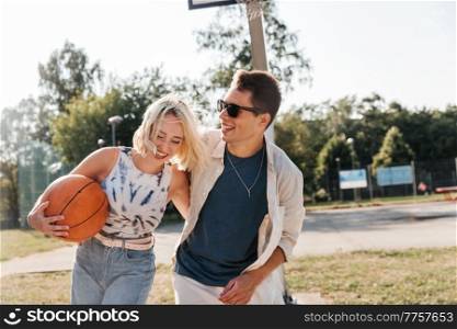 summer holidays, love and people concept - happy young couple with ball on basketball playground. happy couple with ball on basketball playground