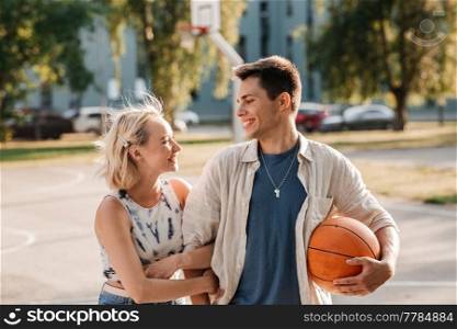 summer holidays, love and people concept - happy young couple with ball on basketball playground. happy couple with ball on basketball playground