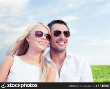 summer holidays, people and dating concept - happy couple in shades over blue sky and grass background
