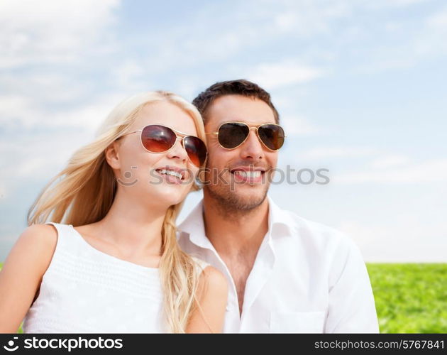 summer holidays, people and dating concept - happy couple in shades over blue sky and grass background