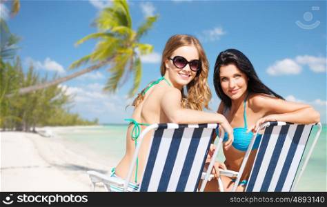 summer holidays, people, leisure, vacation and travel concept - happy women sunbathing in chairs over exotic tropical beach with palm trees and sea shore background
