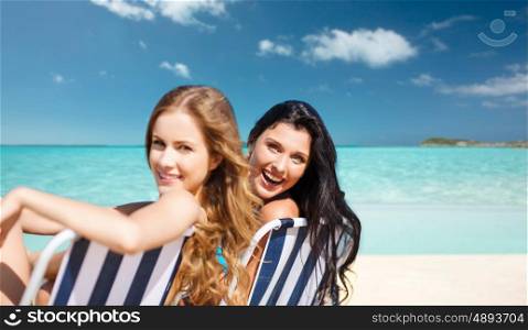 summer holidays, people, leisure, vacation and travel concept - happy women sunbathing in chairs over exotic tropical beach background