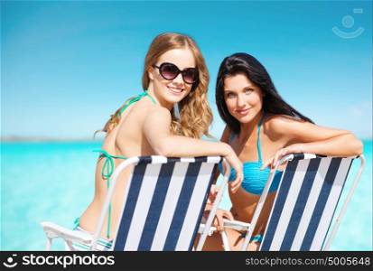 summer holidays, people, leisure, vacation and travel concept - happy women sunbathing in chairs on beach over sea and blue sky background. happy women sunbathing in chairs on summer beach