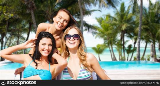 summer holidays, people, leisure, vacation and travel concept - happy women sunbathing in chairs over exotic tropical beach with palm trees and pool background. happy women sunbathing in chairs on summer beach