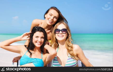 summer holidays, people, leisure, vacation and travel concept - happy women sunbathing on chairs over exotic tropical beach background. happy women sunbathing on chairs over summer beach